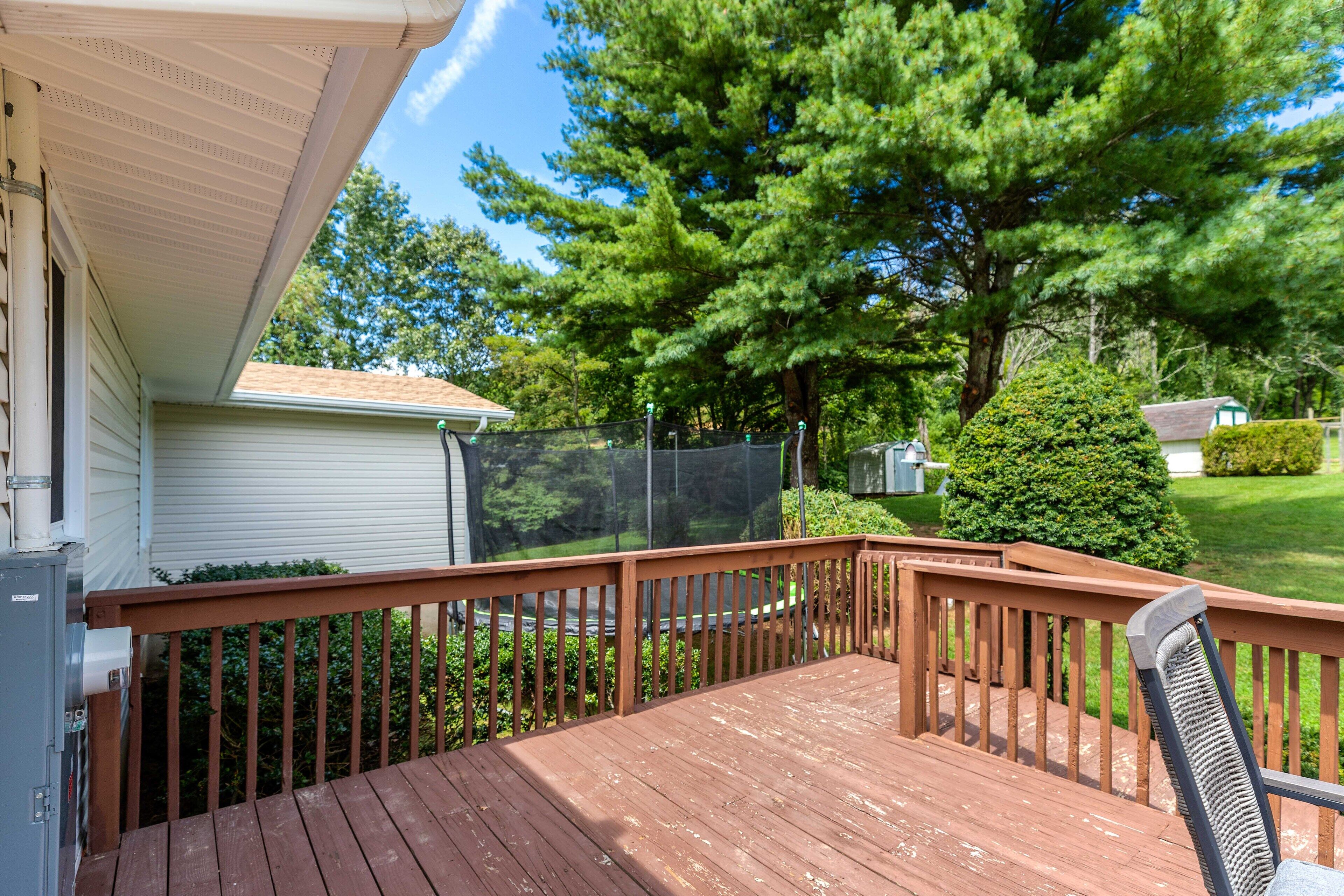 A wooden deck with a railing, a chair, and a view of a green lawn and trees.