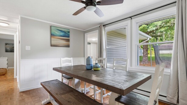 Un coin repas avec une table et des bancs en bois, un ventilateur de plafond et une vue à travers une porte-fenêtre coulissante.