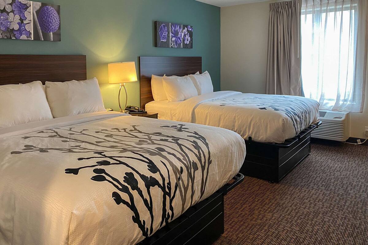 A hotel room with two beds, a nightstand with a lamp, a wall-mounted phone, and a window with curtains.