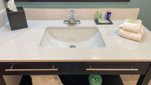 Baño con lavamanos blanco, tocador negro y un cubo de basura verde.