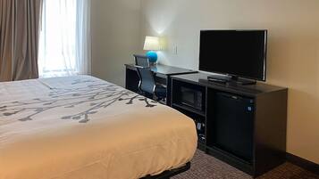Quarto de hotel com uma cama, uma escrivaninha com luminária, televisão e micro-ondas.