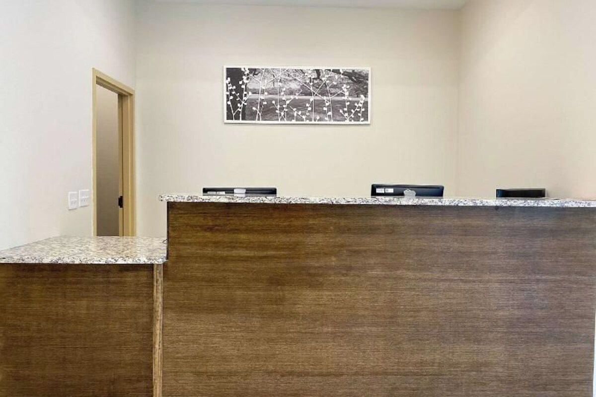 Un comptoir d’accueil avec un revêtement en bois, une œuvre d’art encadrée au-dessus, et une porte sur la gauche.