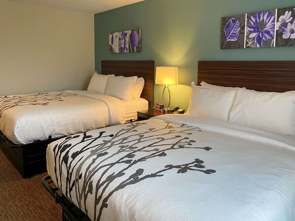 A hotel room with two beds, each with white bedding and a tree branch design. There is a nightstand with a lamp and a phone.