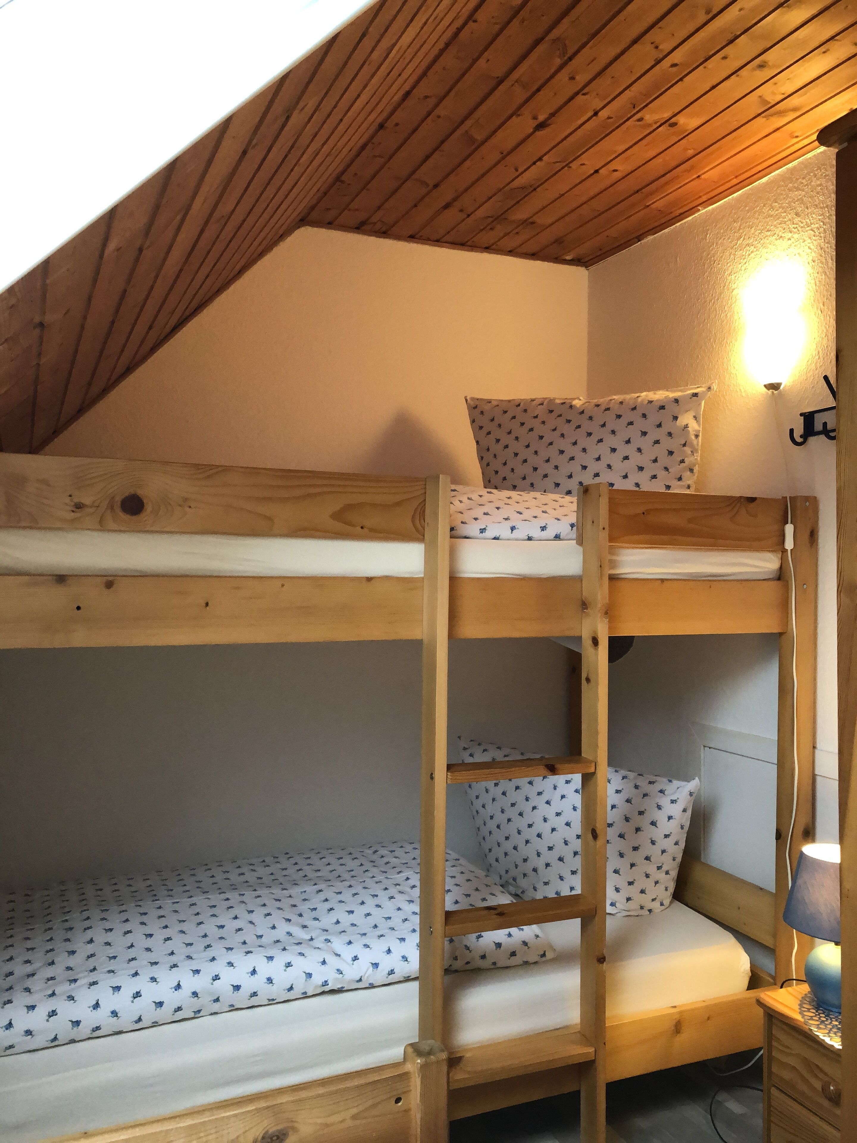 A bunk bed with a wooden ladder, patterned pillows, and a wall-mounted lamp.