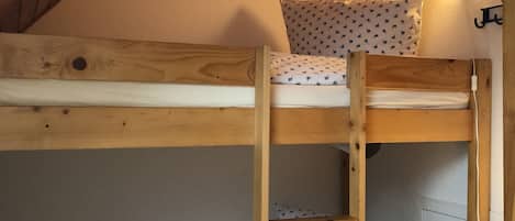 A bunk bed with a wooden ladder, patterned pillows, and a wall-mounted lamp.