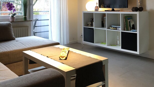 A modern living room with a wooden ceiling, a sofa, a coffee table, a TV on a white shelf, and a window with curtains. - Very nice camp, close to a large playground, swimming pool, sight-seeing dog station (Norden)