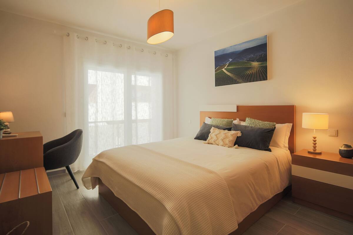 A neatly arranged hotel room with a large bed, a desk, and a chair.
