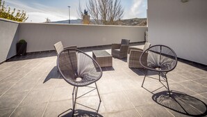 Una terraza en la azotea con dos sillones de mimbre, una mesita y una planta en maceta.