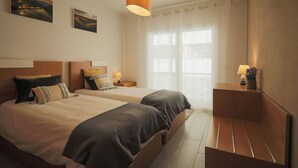 Habitación de hotel con dos camas, una mesita de noche con lámpara, un pequeño banco y una obra de arte en la pared.