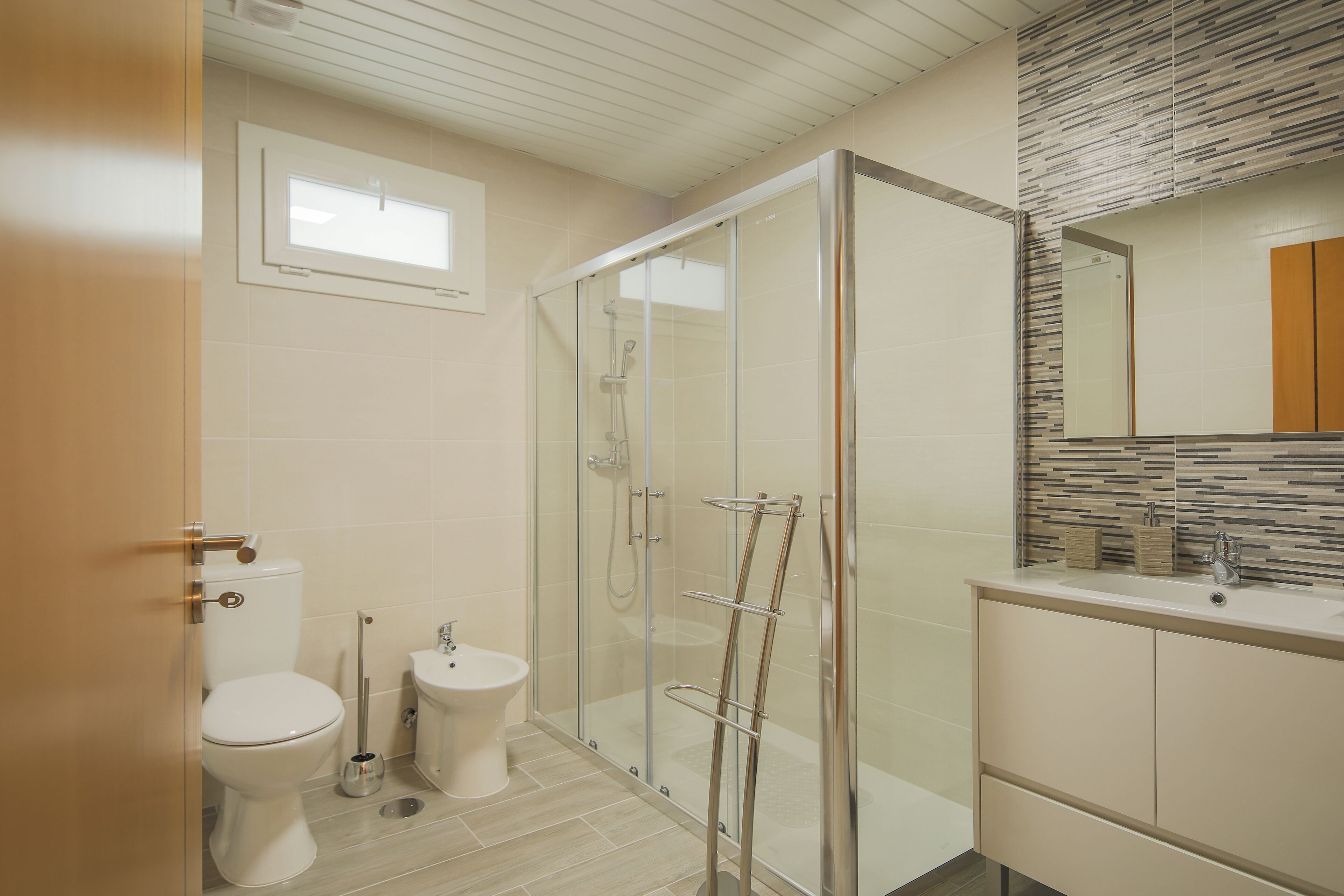 Un baño moderno con ducha de vidrio, inodoro y lavabo con espejo superior.