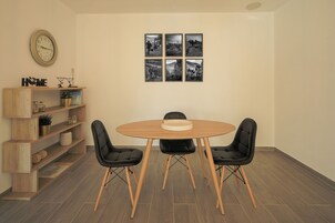 A dining area with a round wooden table, four black chairs, a wooden bookshelf, and a wall clock.