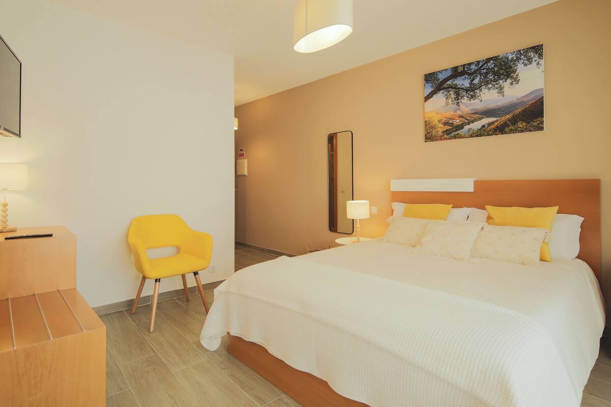 A hotel room with a large bed, a desk with a chair, a TV, and a painting on the wall.