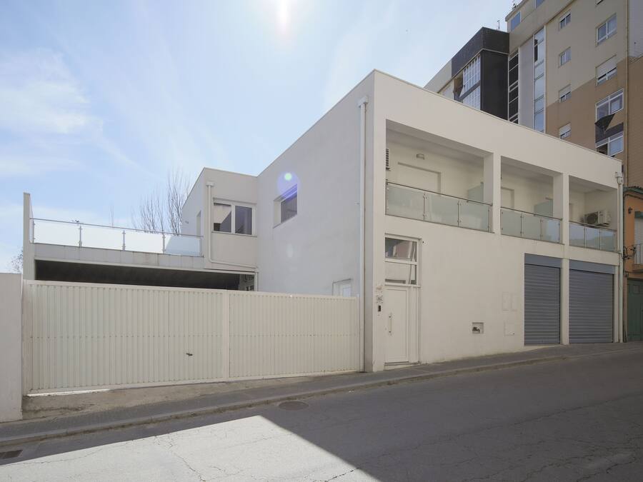 A modern two-story building with a flat roof, a gated entrance, and a balcony on the upper floor.