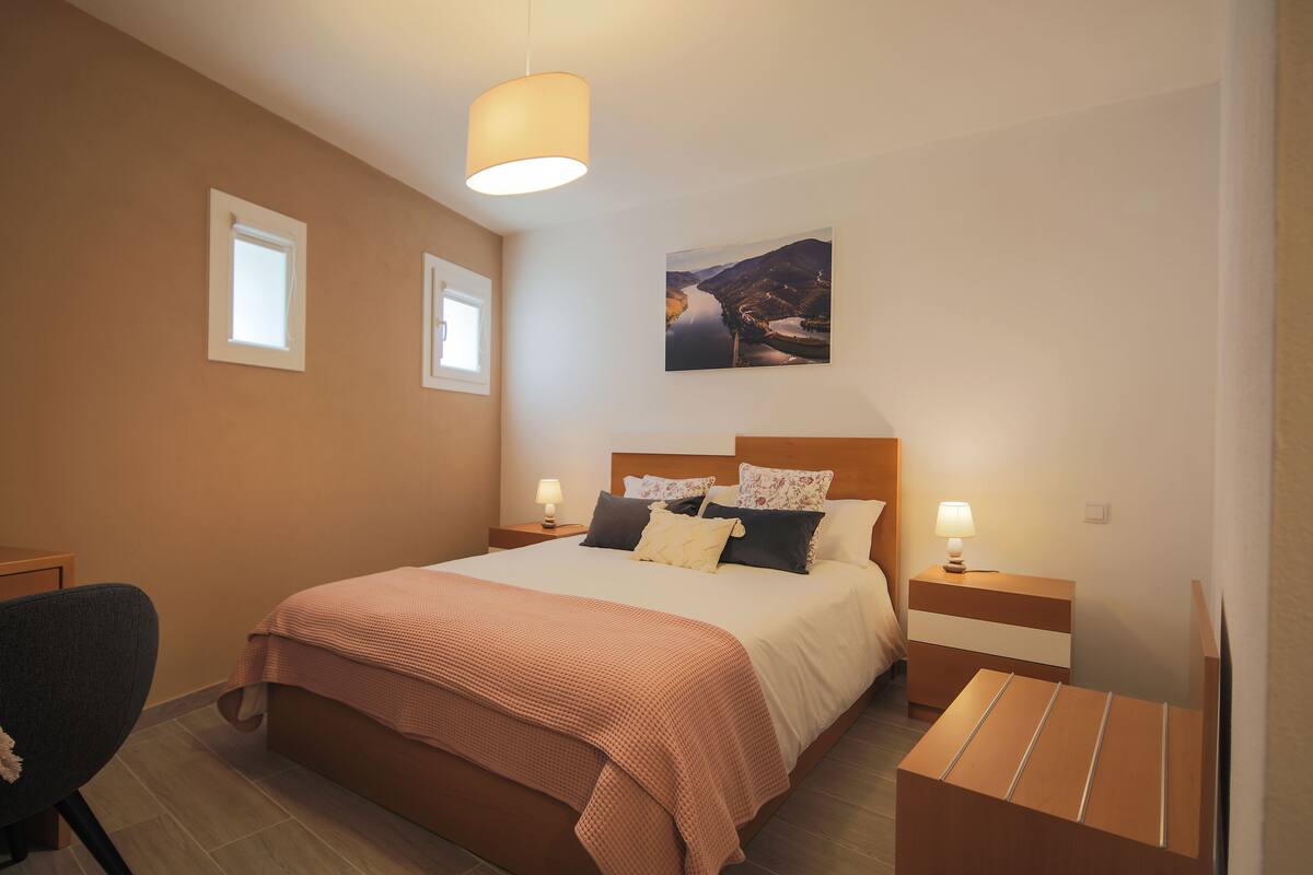 A bedroom with a large bed, two bedside tables with lamps, a chair, and a painting on the wall.