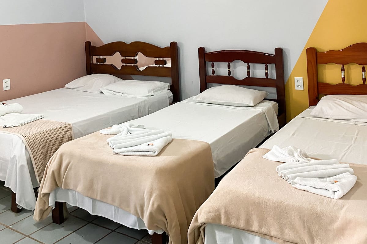 A hotel room with three single beds, each with a wooden headboard and white bedding.