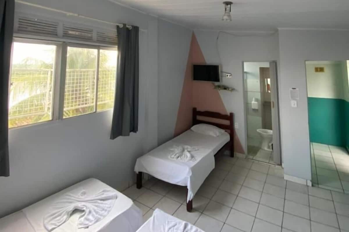 A room with two single beds, a TV mounted on the wall, and a bathroom visible through an open door.