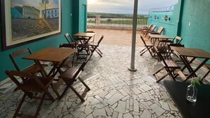 A covered outdoor seating area with tables and chairs, a tiled floor, and a mural on the wall. - Pousada Vila do Penedo (Penedo)