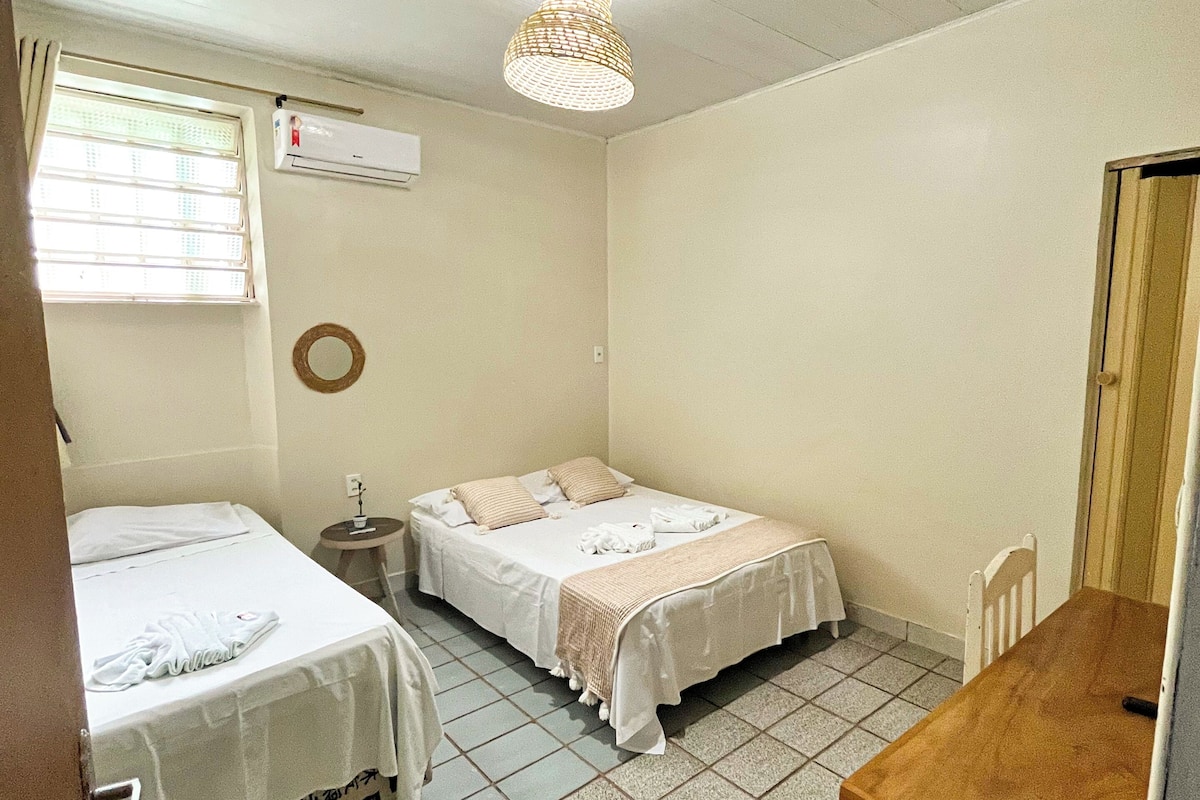 A small, clean room with two beds, a table, and a ceiling fan.