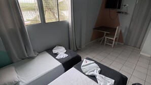 A room with two single beds, a small table, a chair, a TV mounted on the wall, and a window with a view of greenery. - Pousada Vila do Penedo (Penedo)