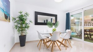 Un comedor moderno con una mesa de vidrio, sillas blancas, un espejo grande y una planta en maceta.