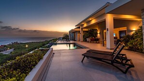 A modern resort with a pool, outdoor seating, and a view of the ocean at dusk. - Stunning Luxury Villa/ Private Infinity Pool with Panoramic Sea Views (Sint Willibrordus)