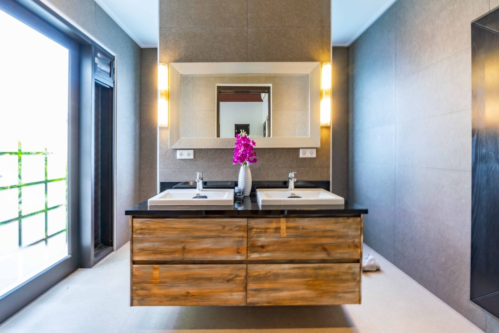 A modern bathroom with a double sink vanity, wooden drawers, and a large mirror with wall-mounted lights.