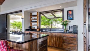A modern kitchen with a large island, wooden cabinetry, and a view of greenery outside. - Stunning Luxury Villa/ Private Infinity Pool with Panoramic Sea Views (Sint Willibrordus)