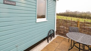 A blue cottage with a sign reading "Robins Nest," a window, a wicker fence, and a metal table with chairs outside. - Robins Nest (Southam)