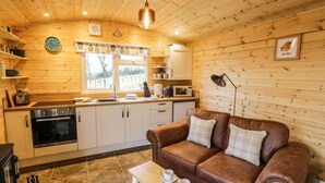 A cozy cabin interior with a wooden interior, a kitchen with modern appliances, a brown leather sofa, and a small table with cups. - Robins Nest (Southam)