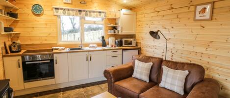 A cozy cabin interior with a wooden interior, a kitchen with modern appliances, a brown leather sofa, and a small table with cups.