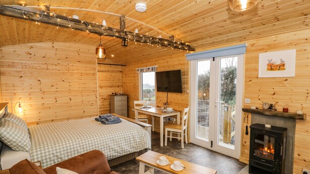 A cozy cabin with a bed, sofa, fireplace, dining area, and a TV. - Robins Nest (Southam)