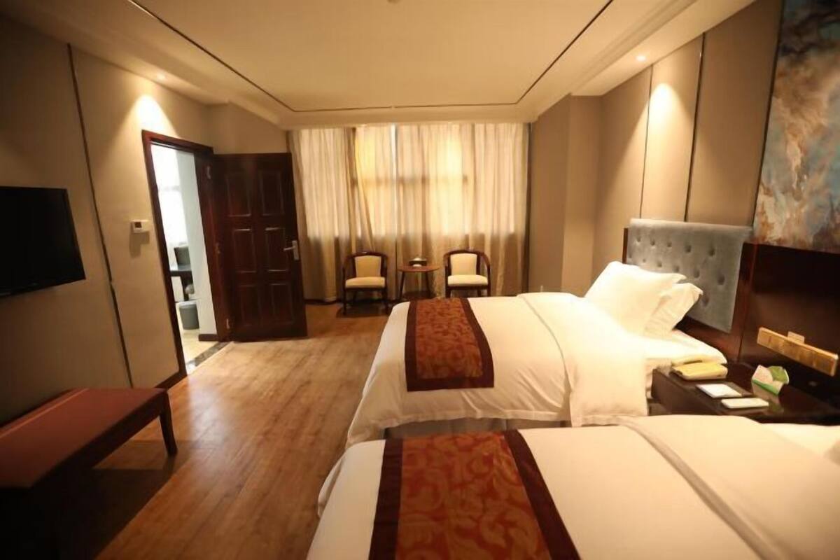 A hotel room with two beds, a desk, a chair, a television, and a large window with curtains.