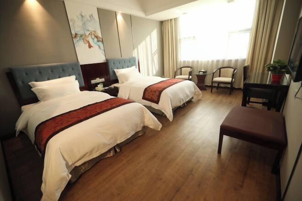 A hotel room with two beds, a desk, a chair, and a large window with curtains.