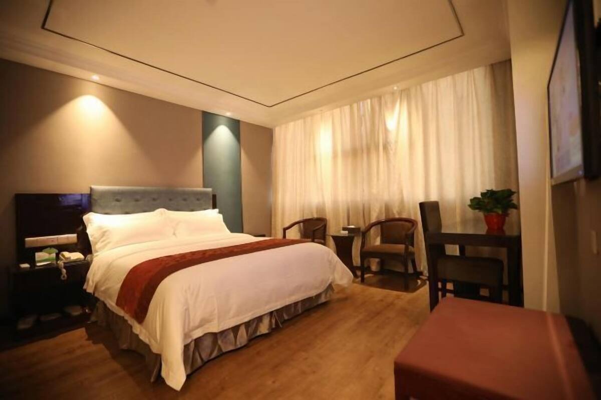A hotel room with a bed, a desk, a chair, a TV, and a window with curtains.