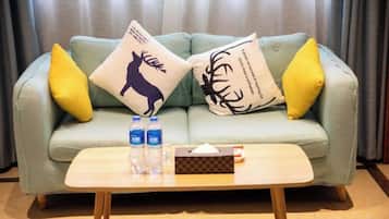 A light green sofa with two yellow pillows and two decorative pillows with animal silhouettes. A wooden coffee table with a tissue box and two bottles is in front.