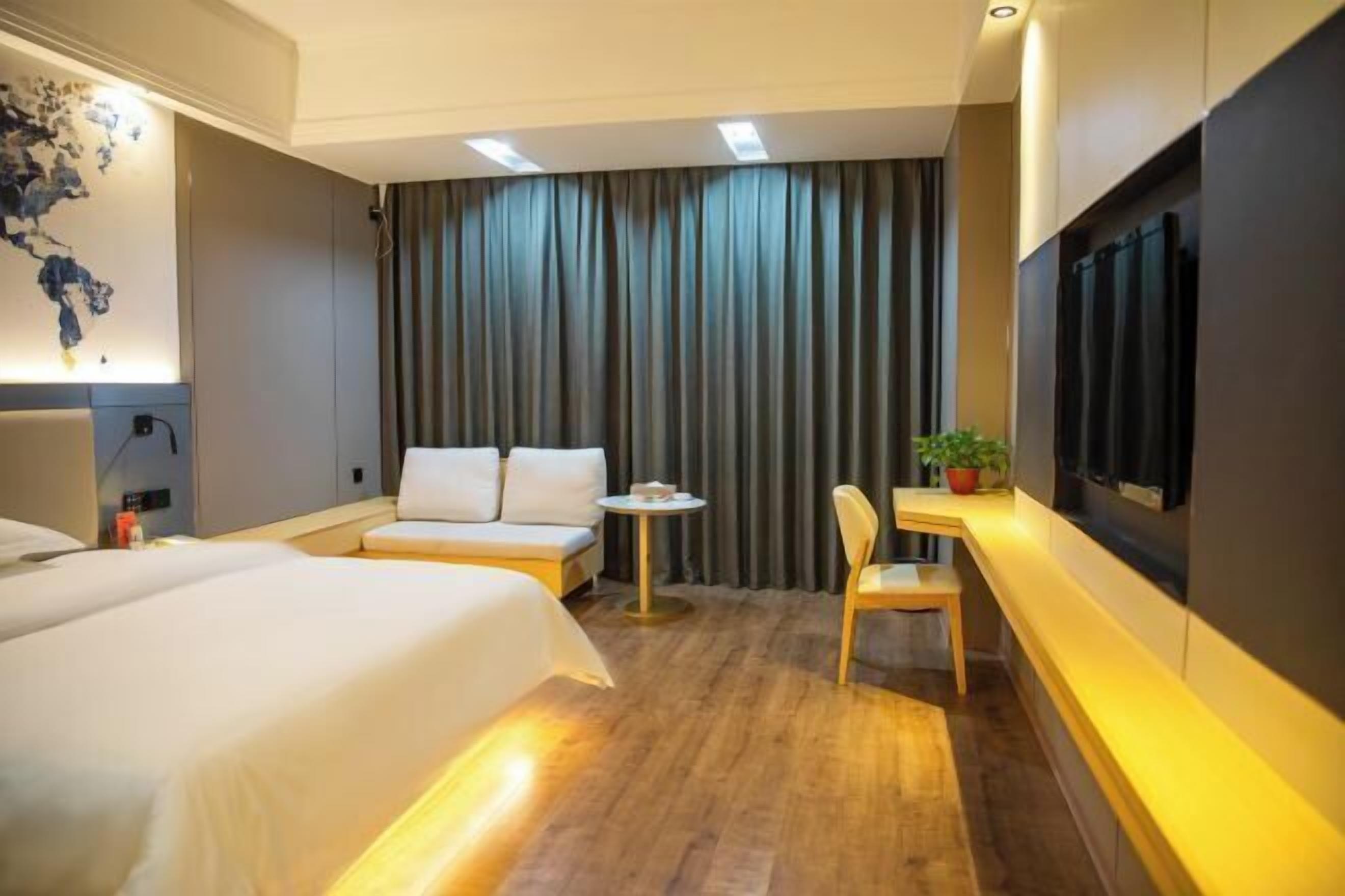 Une chambre d’hôtel avec deux lits, une petite table, une chaise, un téléviseur fixé au mur et une grande fenêtre avec des rideaux.