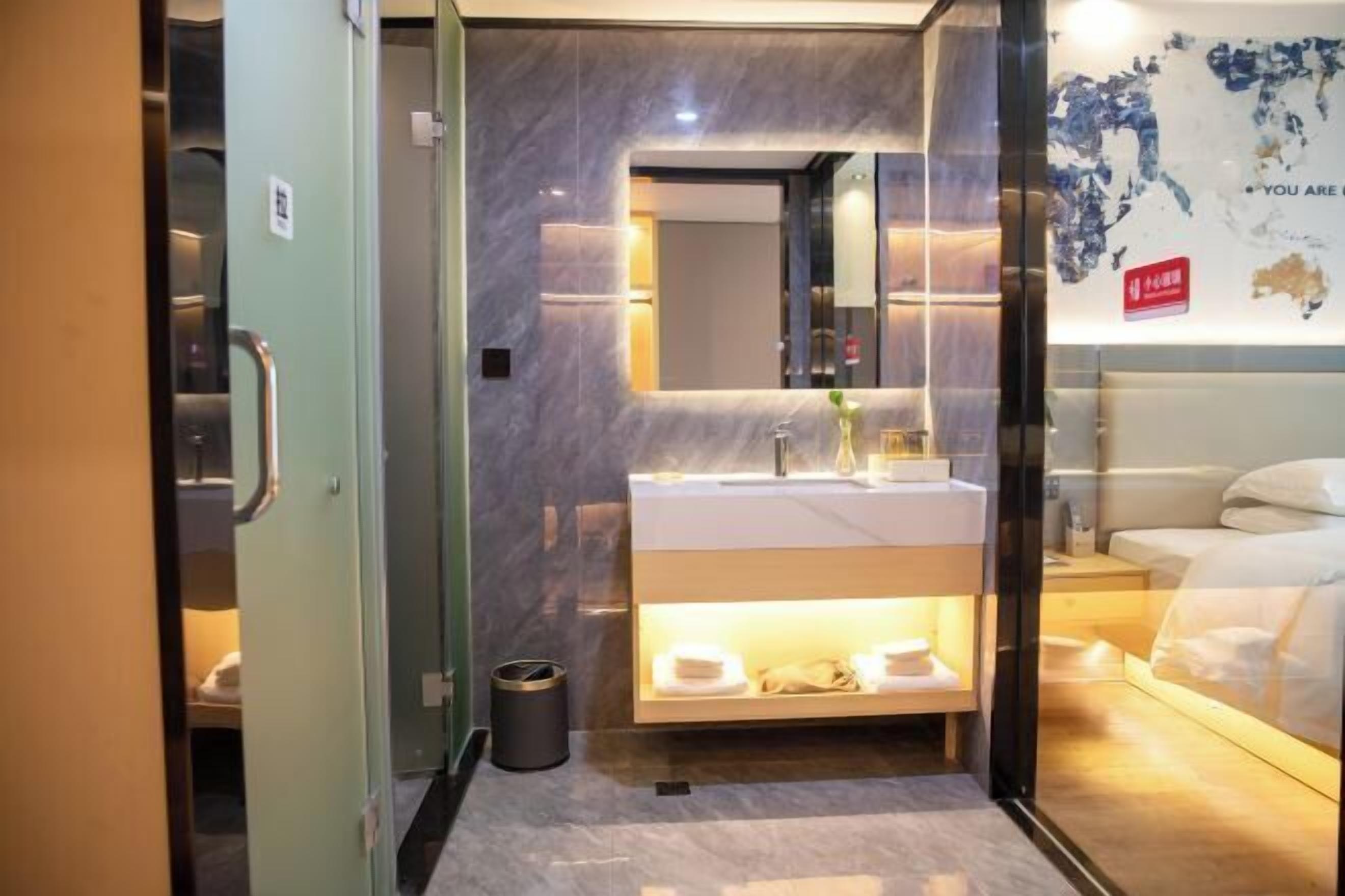 Een moderne hotelkamer met een glazen scheidingswand, een betegelde marmeren muur, een groot bed, een nachtkastje en een spiegel aan de muur.