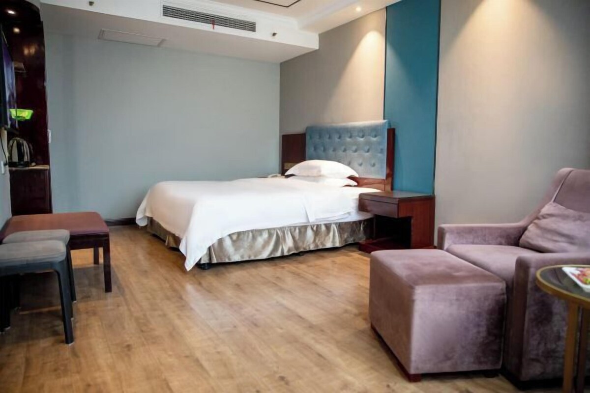 A hotel room with a bed, a seating area with a chair and ottoman, a small table, and a wall-mounted TV.