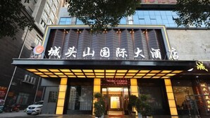 A hotel entrance with a sign in Chinese characters, a covered entrance area, and potted plants. - Chengtoushan International Hotel (Li County)