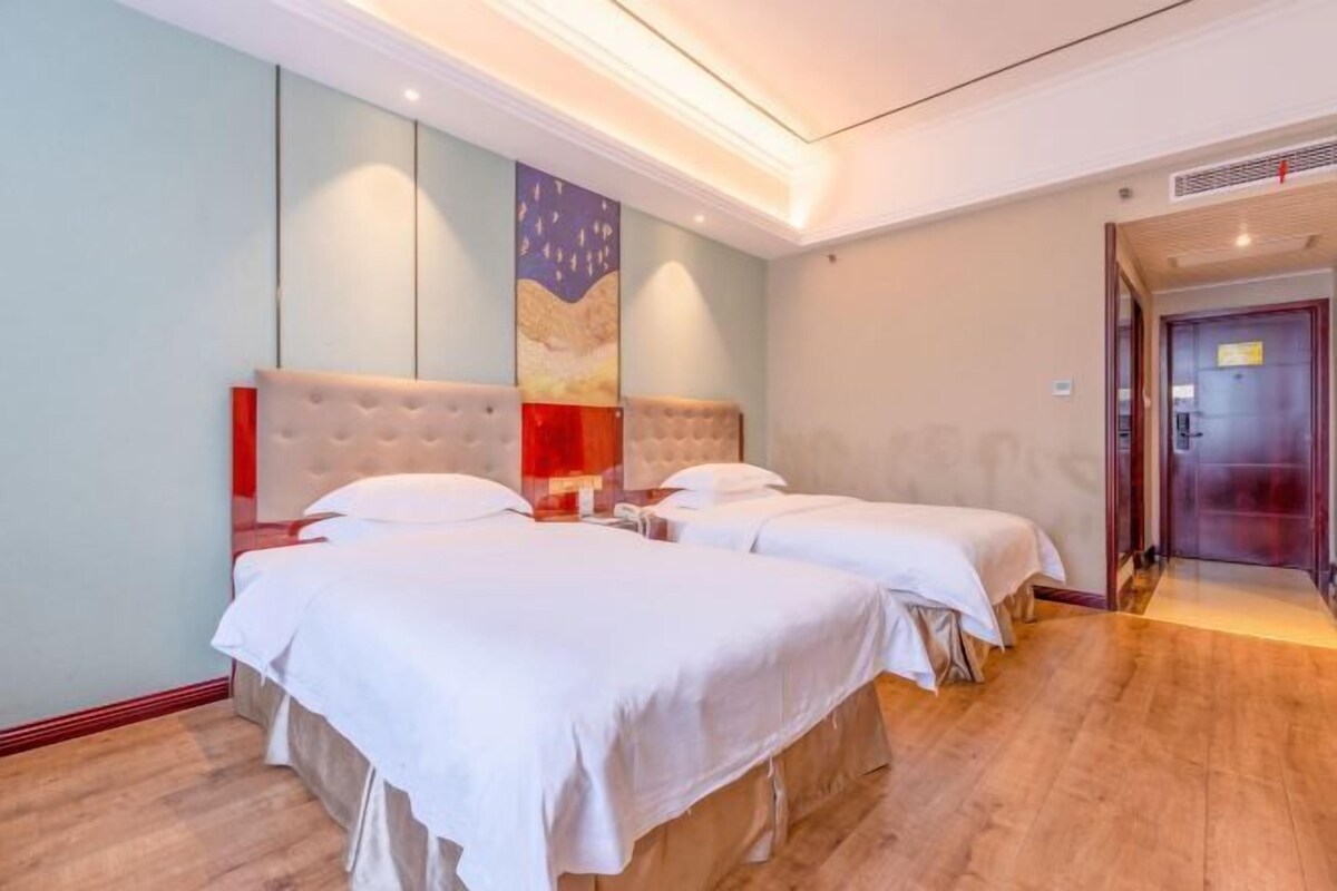 A hotel room with two beds, a large painting on the wall, and a wooden floor.