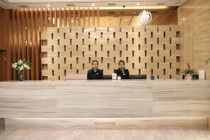 A reception desk with a wooden panel wall, two receptionists, and a potted plant. - Chengtoushan International Hotel (Li County)