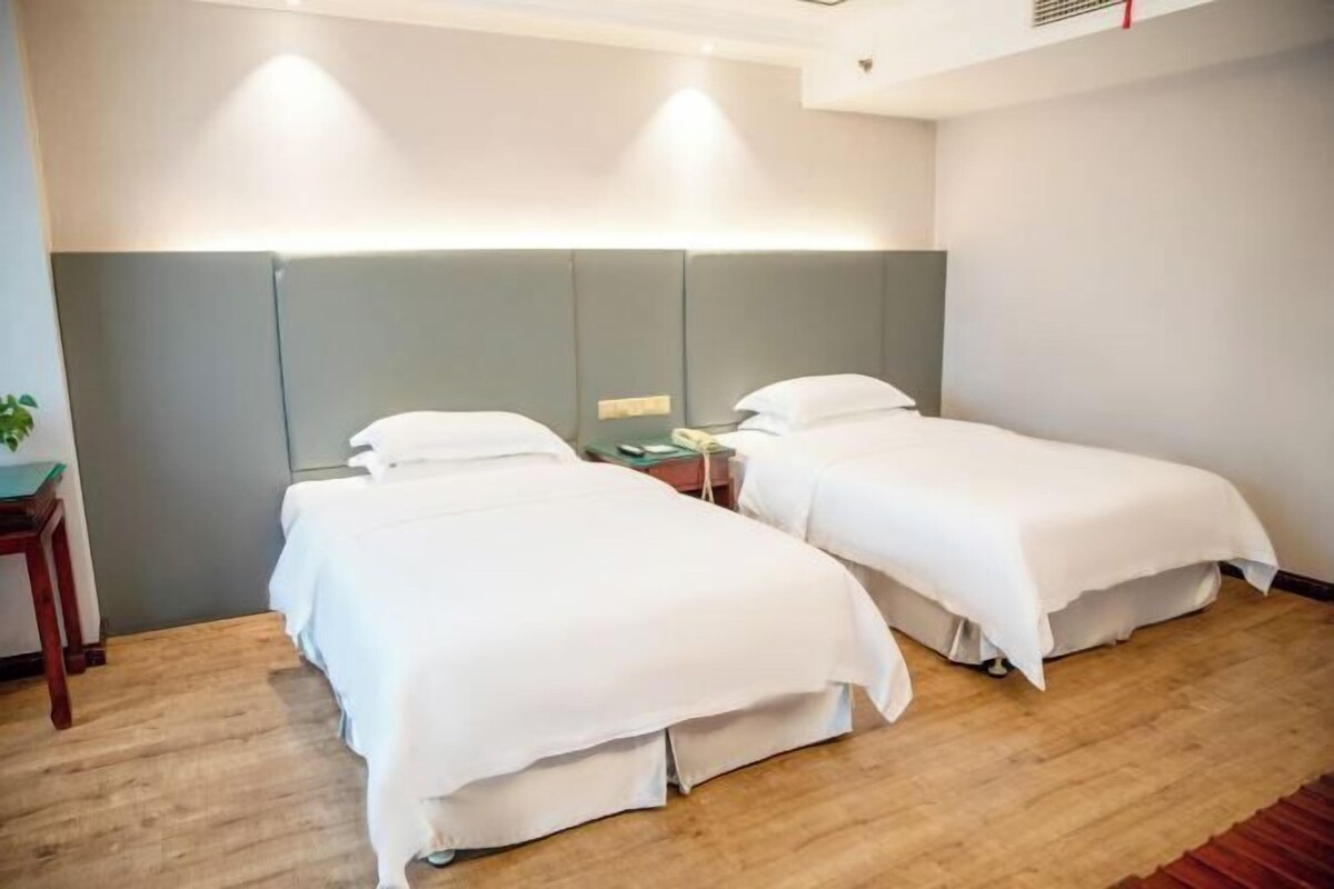 A hotel room with two single beds, a wooden floor, a nightstand with a lamp, and a small table with a plant.