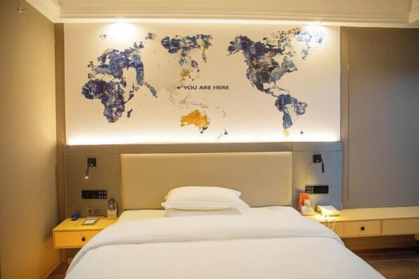 Une chambre d’hôtel avec un grand lit, une table de chevet, une petite table d’appoint, une œuvre d’art représentant une carte du monde accrochée au mur et une tête de lit.