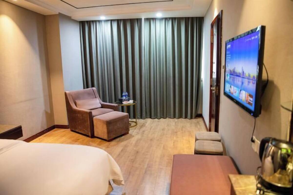 A hotel room with a bed, a sofa, a television, and a curtain.