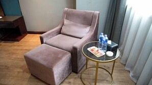 A room with a brown armchair and ottoman, a small round table with a magazine and water bottles, and a wooden floor. - Chengtoushan International Hotel (Li County)