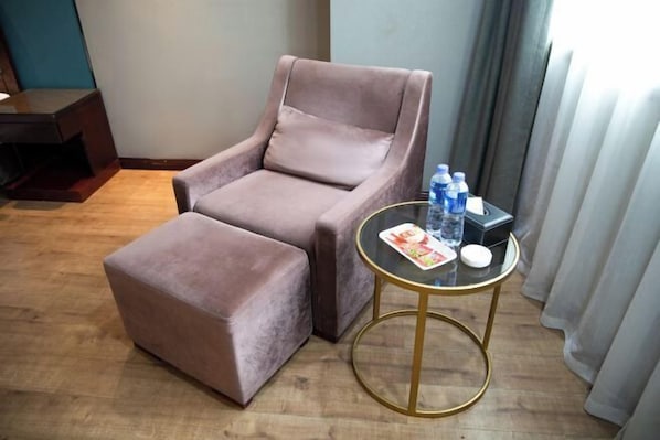 A room with a brown armchair and ottoman, a small round table with a magazine and water bottles, and a wooden floor. - Chengtoushan International Hotel (Li County)