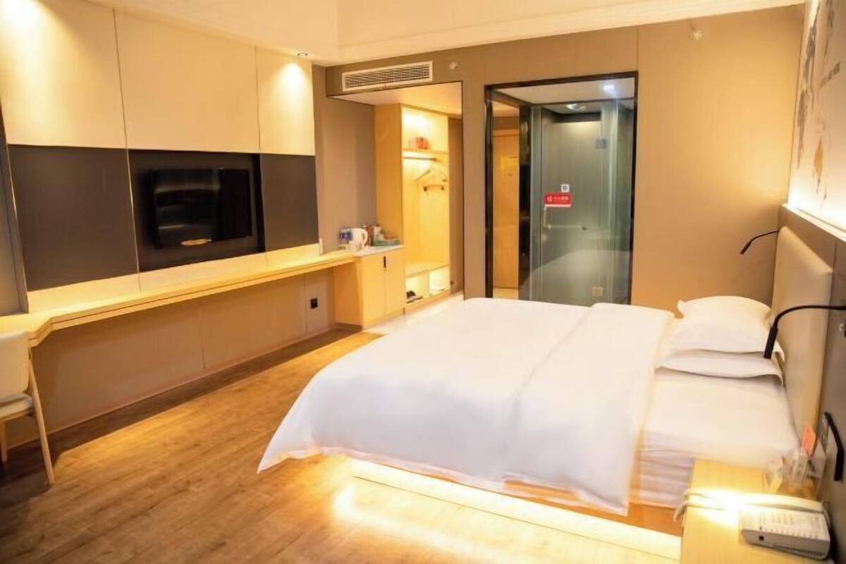 A hotel room with a bed, a desk with a computer, a television, and a bathroom door.