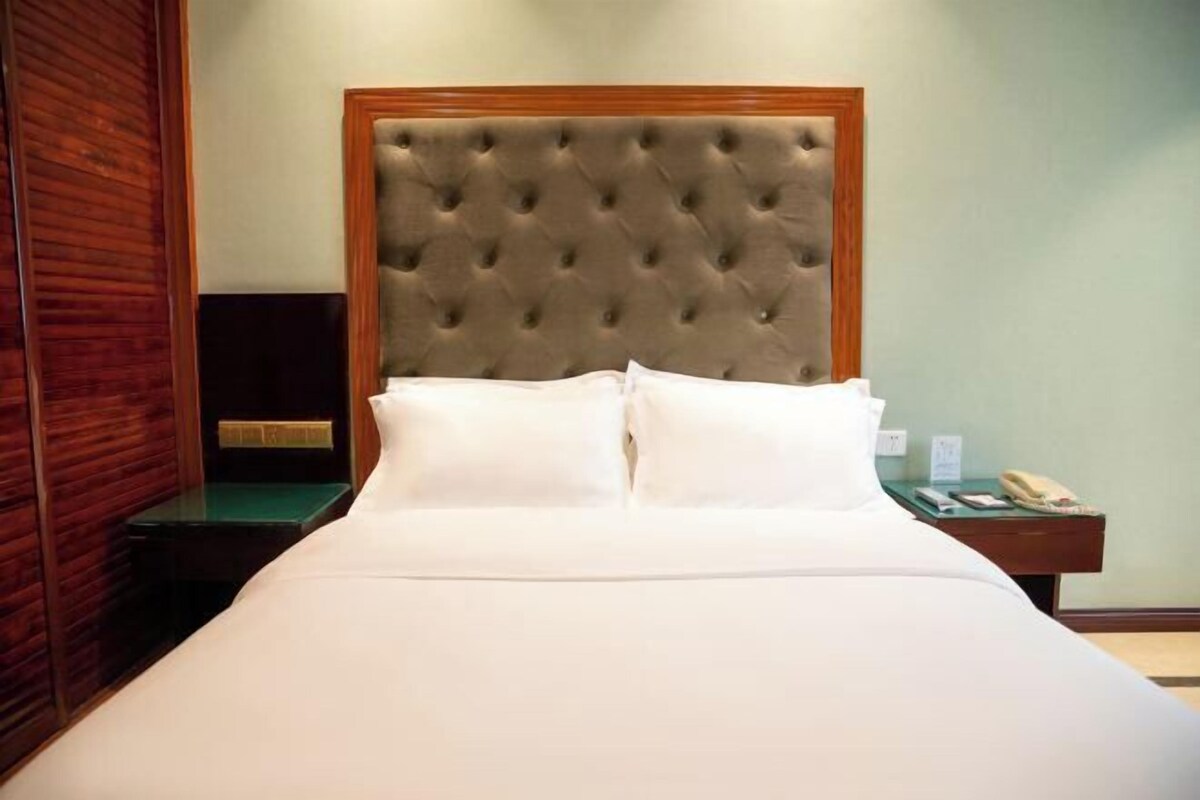 A hotel room with a tufted headboard, a green side table, and a bedside telephone.