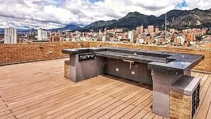 Zona cucina esterna con piano in pietra e barbecue integrato, con vista su una città e montagne sullo sfondo.