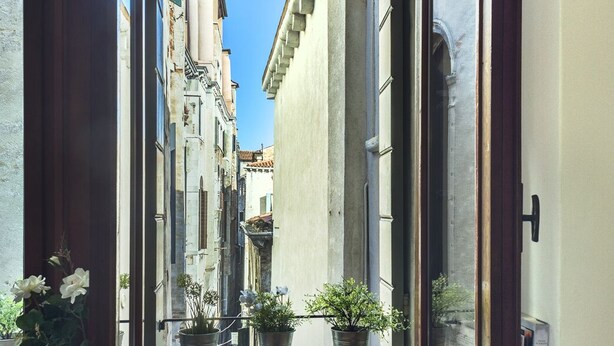 A room with a window overlooking a narrow street. There are three potted plants on the windowsill. - ACQUARELLO, SPACIOUS APARTMENT IN THE HEART OF VENICE (Venise)